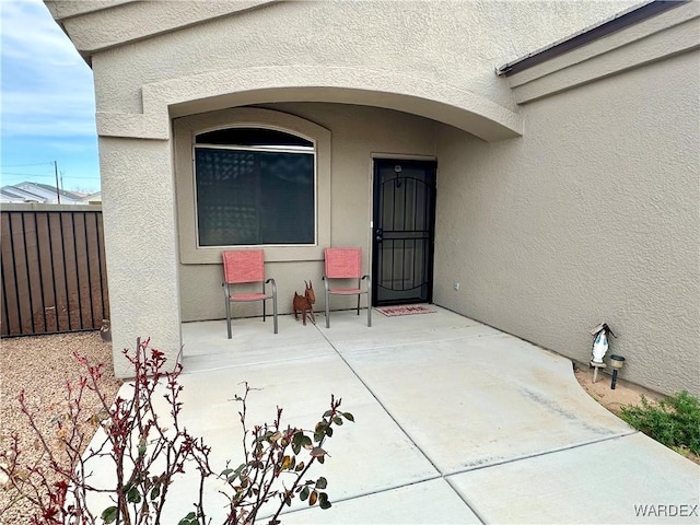 view of exterior entry with a patio, fence, and stucco siding