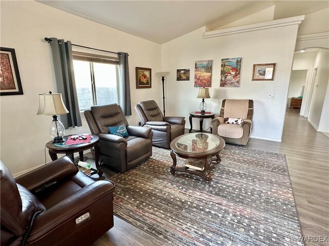 living area with lofted ceiling, baseboards, arched walkways, and wood finished floors