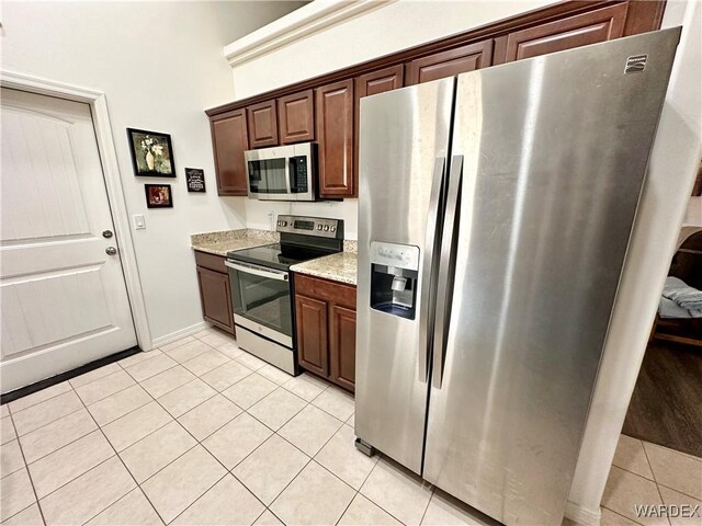 kitchen featuring dark brown cabinetry, appliances with stainless steel finishes, light stone counters, and light tile patterned flooring