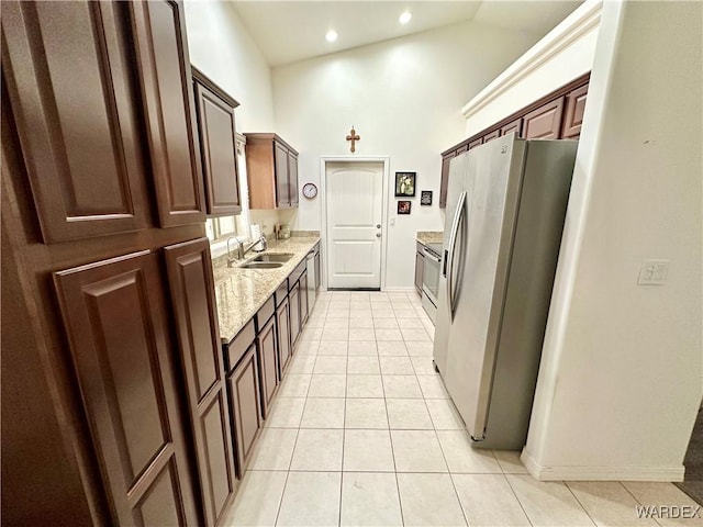 kitchen with light tile patterned floors, appliances with stainless steel finishes, light stone counters, high vaulted ceiling, and a sink