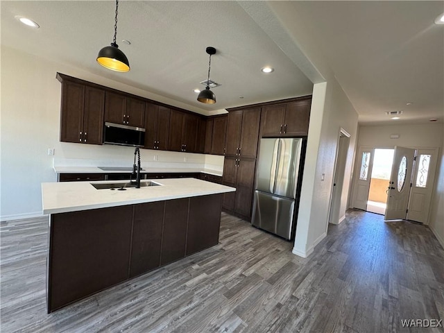 kitchen with stainless steel appliances, a sink, light countertops, an island with sink, and decorative light fixtures