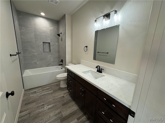 full bath with shower / bath combination, visible vents, toilet, wood finished floors, and vanity