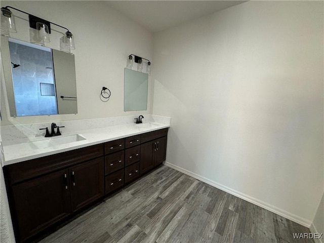 full bath with double vanity, wood finished floors, a sink, and baseboards