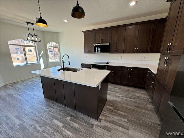 kitchen with a kitchen island with sink, a sink, light countertops, stainless steel microwave, and pendant lighting