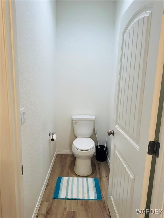bathroom with toilet, baseboards, and wood finished floors