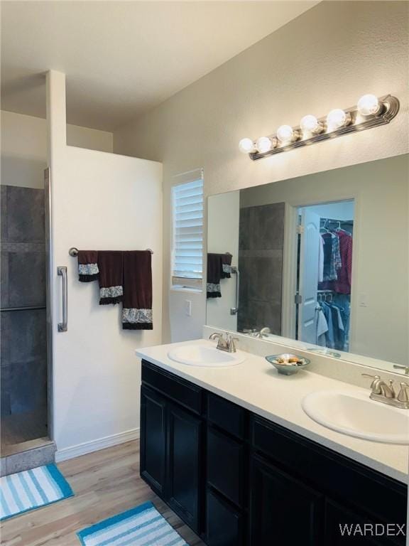 full bath with double vanity, a sink, a walk in shower, and wood finished floors