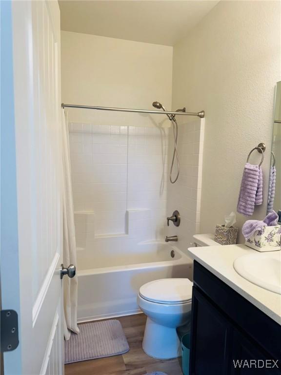bathroom featuring toilet, shower / bathtub combination with curtain, wood finished floors, and vanity