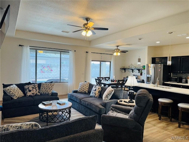 living area with visible vents, light wood finished floors, and ceiling fan