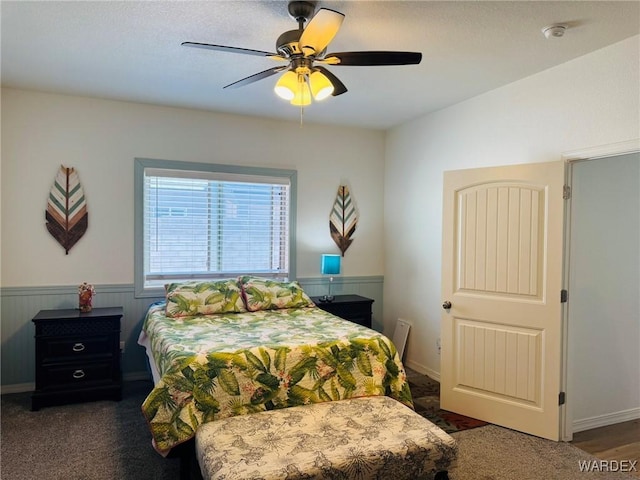 carpeted bedroom with ceiling fan and wainscoting