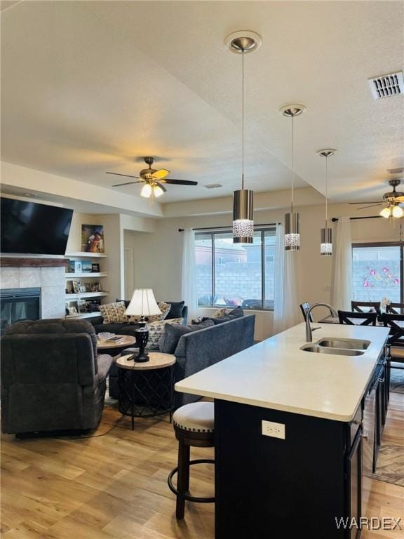 kitchen with ceiling fan, a sink, light countertops, open floor plan, and light wood-style flooring