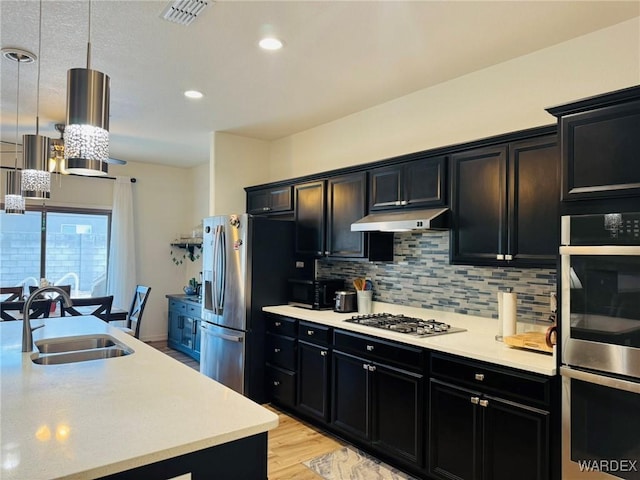 kitchen featuring appliances with stainless steel finishes, a sink, light countertops, dark cabinets, and under cabinet range hood