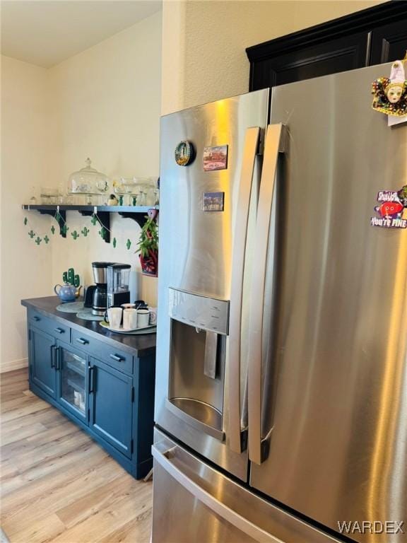 kitchen with dark countertops, open shelves, stainless steel fridge, light wood finished floors, and blue cabinets