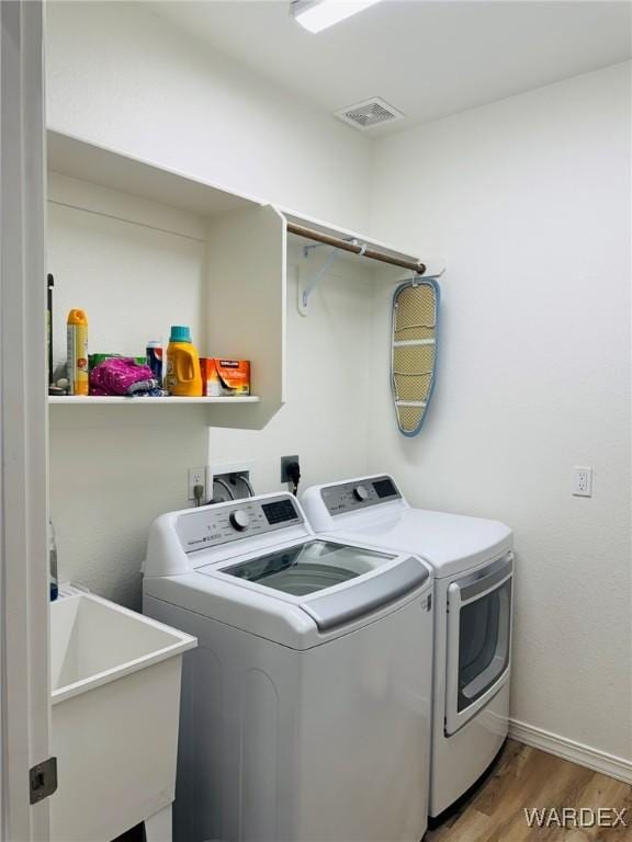 laundry area featuring laundry area, a sink, separate washer and dryer, wood finished floors, and visible vents