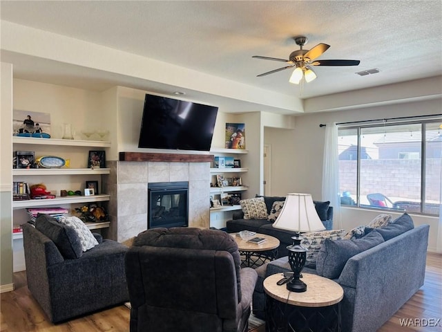 living area with visible vents, wood finished floors, a fireplace, ceiling fan, and a textured ceiling
