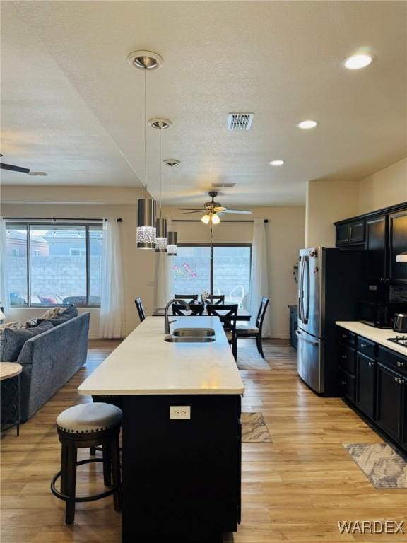 kitchen featuring a ceiling fan, visible vents, a sink, open floor plan, and dark cabinets