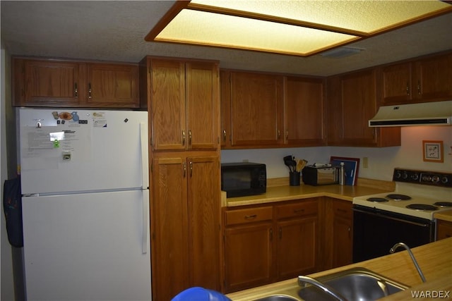 kitchen featuring white appliances, brown cabinetry, light countertops, under cabinet range hood, and a sink