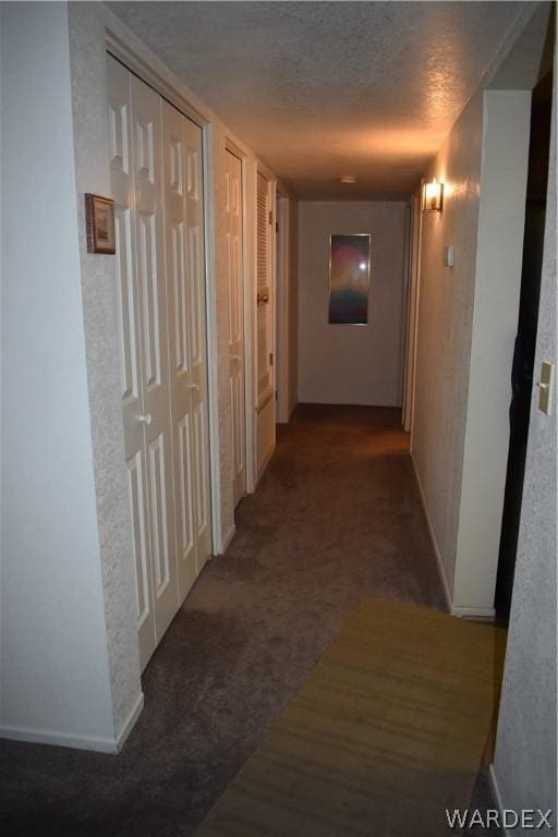 hall with baseboards, dark carpet, and a textured ceiling