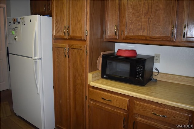 kitchen featuring black microwave, light countertops, freestanding refrigerator, and brown cabinets