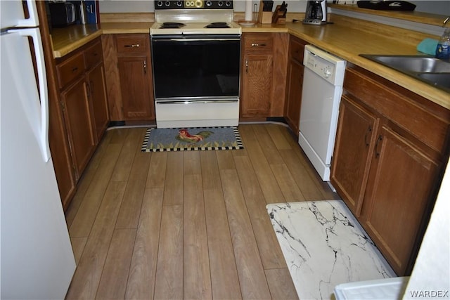 kitchen with white appliances, a sink, light wood-style floors, light countertops, and brown cabinetry