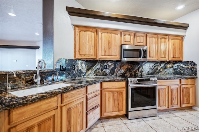 kitchen with a sink, stainless steel appliances, tasteful backsplash, and dark stone countertops