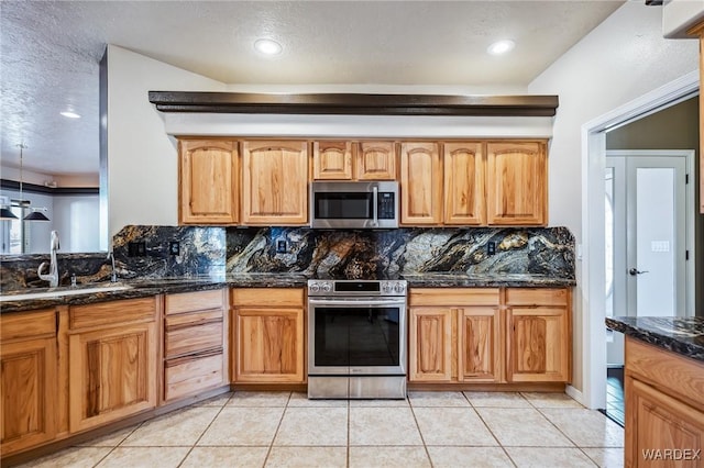kitchen featuring a sink, dark stone counters, light tile patterned flooring, decorative backsplash, and appliances with stainless steel finishes