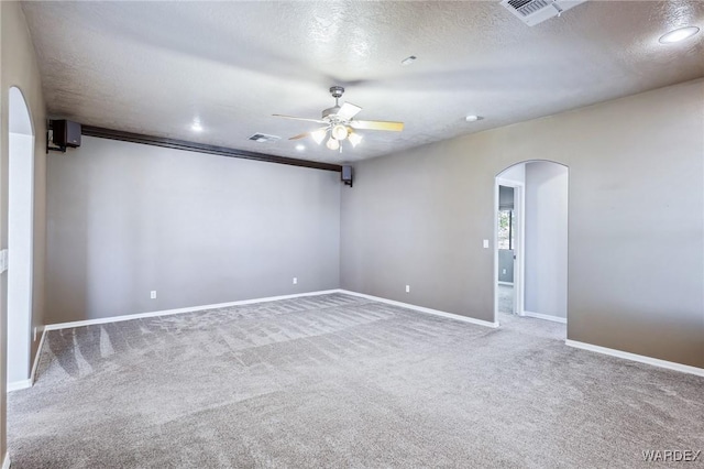 unfurnished room featuring carpet flooring, a textured ceiling, visible vents, ceiling fan, and arched walkways