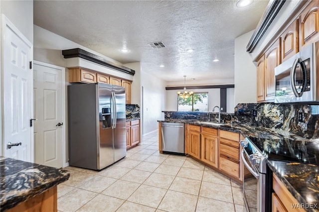 kitchen featuring a peninsula, light tile patterned floors, a sink, visible vents, and appliances with stainless steel finishes