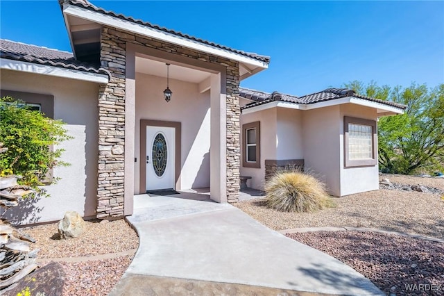 property entrance with a tile roof, stucco siding, and stone siding
