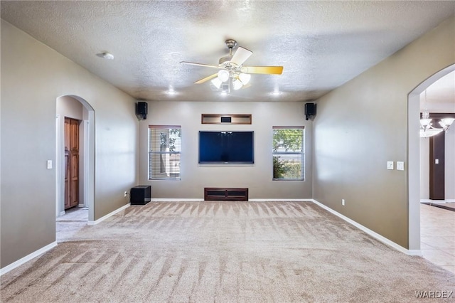 unfurnished living room with arched walkways, a textured ceiling, a ceiling fan, and carpet