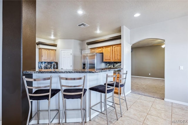 kitchen featuring a breakfast bar area, stainless steel refrigerator with ice dispenser, visible vents, arched walkways, and light colored carpet