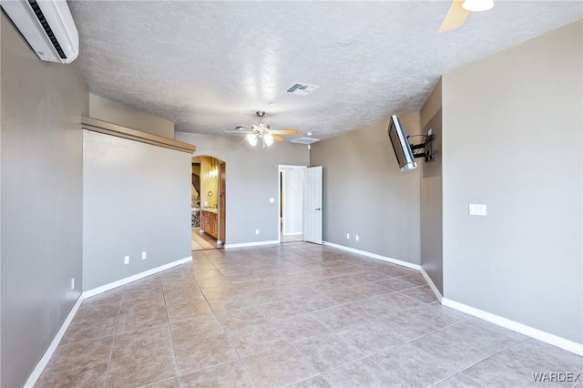 tiled empty room featuring a ceiling fan, a textured ceiling, an AC wall unit, visible vents, and arched walkways
