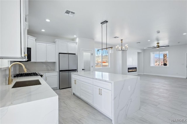 kitchen with visible vents, freestanding refrigerator, a glass covered fireplace, a kitchen island, and a sink