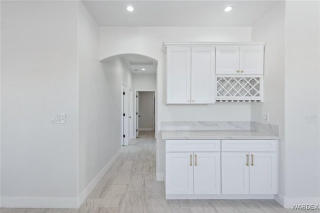 interior space featuring arched walkways, light stone counters, recessed lighting, white cabinetry, and baseboards