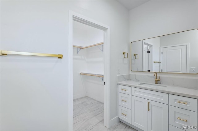 bathroom featuring marble finish floor, baseboards, a walk in closet, and vanity