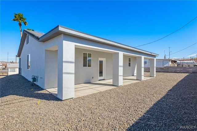 rear view of property featuring a patio area, fence, and stucco siding