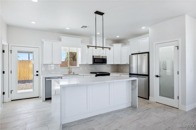 kitchen with visible vents, appliances with stainless steel finishes, white cabinets, a sink, and a kitchen island