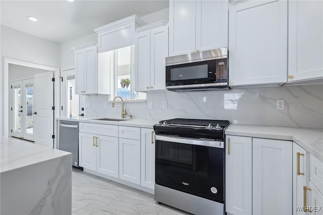 kitchen with marble finish floor, stainless steel appliances, backsplash, white cabinetry, and a sink