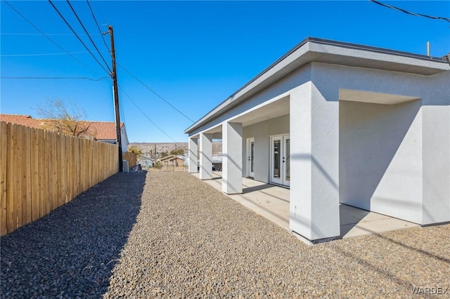 view of home's exterior with french doors, a patio area, fence, and stucco siding