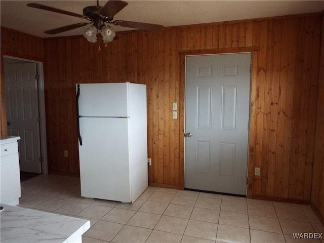 17516 N Ladera Dr, Dolan Springs, AZ 86441 - kitchen with light tile patterned floors, a ceiling fan, freestanding refrigerator, white cabinets, and wood walls