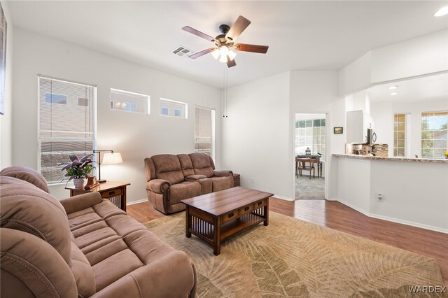 living area featuring light wood-type flooring, a ceiling fan, visible vents, and a wealth of natural light