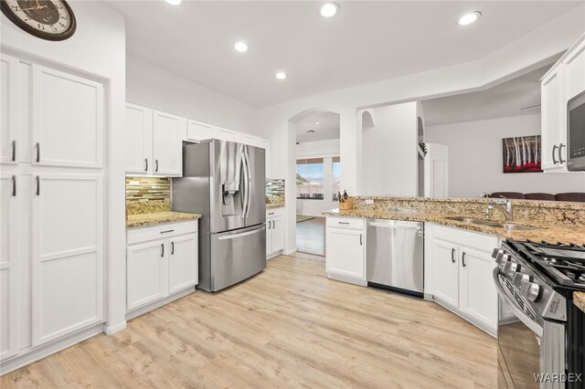 kitchen featuring stainless steel appliances, white cabinetry, light wood-type flooring, light stone countertops, and tasteful backsplash