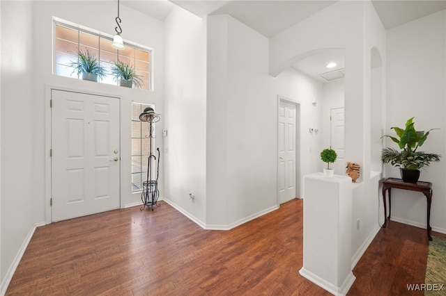 entryway featuring dark wood-style floors, arched walkways, a towering ceiling, and baseboards