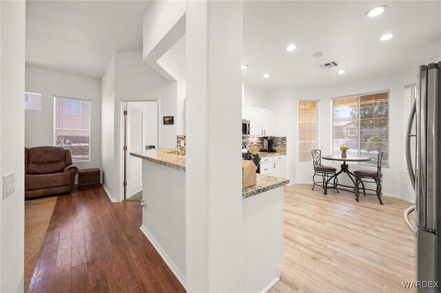 kitchen featuring visible vents, white cabinets, appliances with stainless steel finishes, light stone countertops, and light wood-style floors