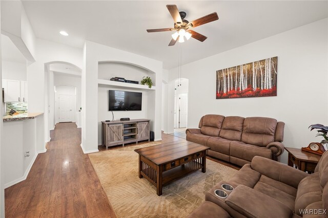 living area featuring arched walkways, recessed lighting, a ceiling fan, baseboards, and light wood-style floors