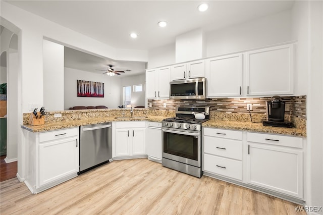 kitchen with arched walkways, a peninsula, a sink, white cabinetry, and appliances with stainless steel finishes