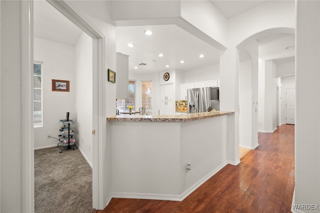 kitchen featuring light stone counters, stainless steel refrigerator with ice dispenser, dark wood-type flooring, white cabinets, and baseboards