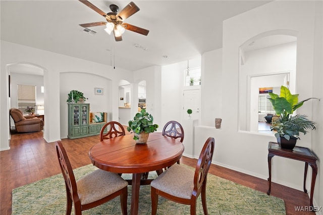 dining area featuring arched walkways, visible vents, a ceiling fan, wood finished floors, and baseboards