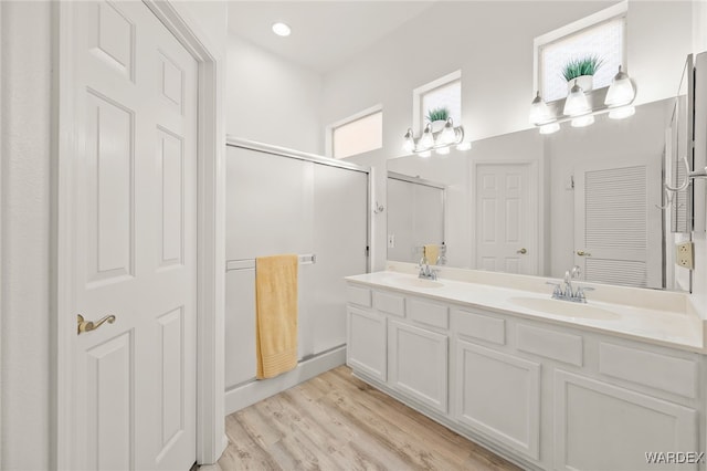 full bathroom with double vanity, a shower stall, a sink, and wood finished floors