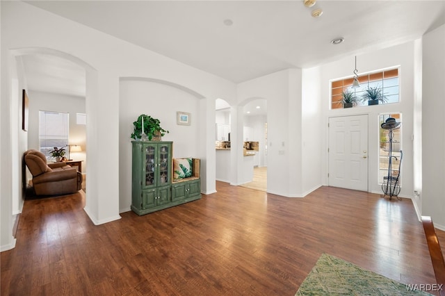 foyer featuring baseboards, arched walkways, and dark wood-type flooring