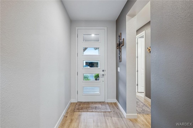 entryway with a textured wall, light wood-type flooring, and baseboards